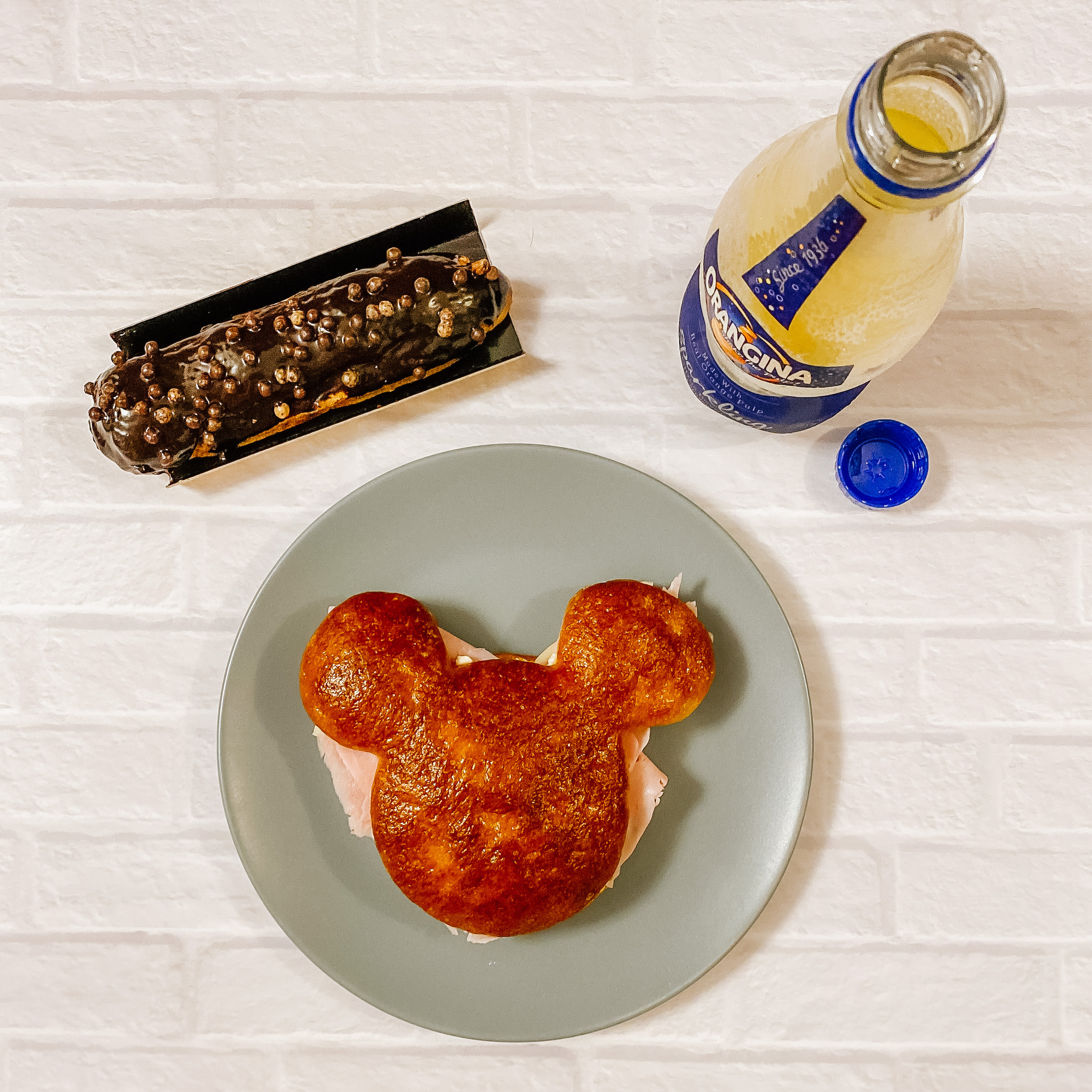 Celebration Mickey Sandwich on a plate, with an eclair, and a bottle of Orangina