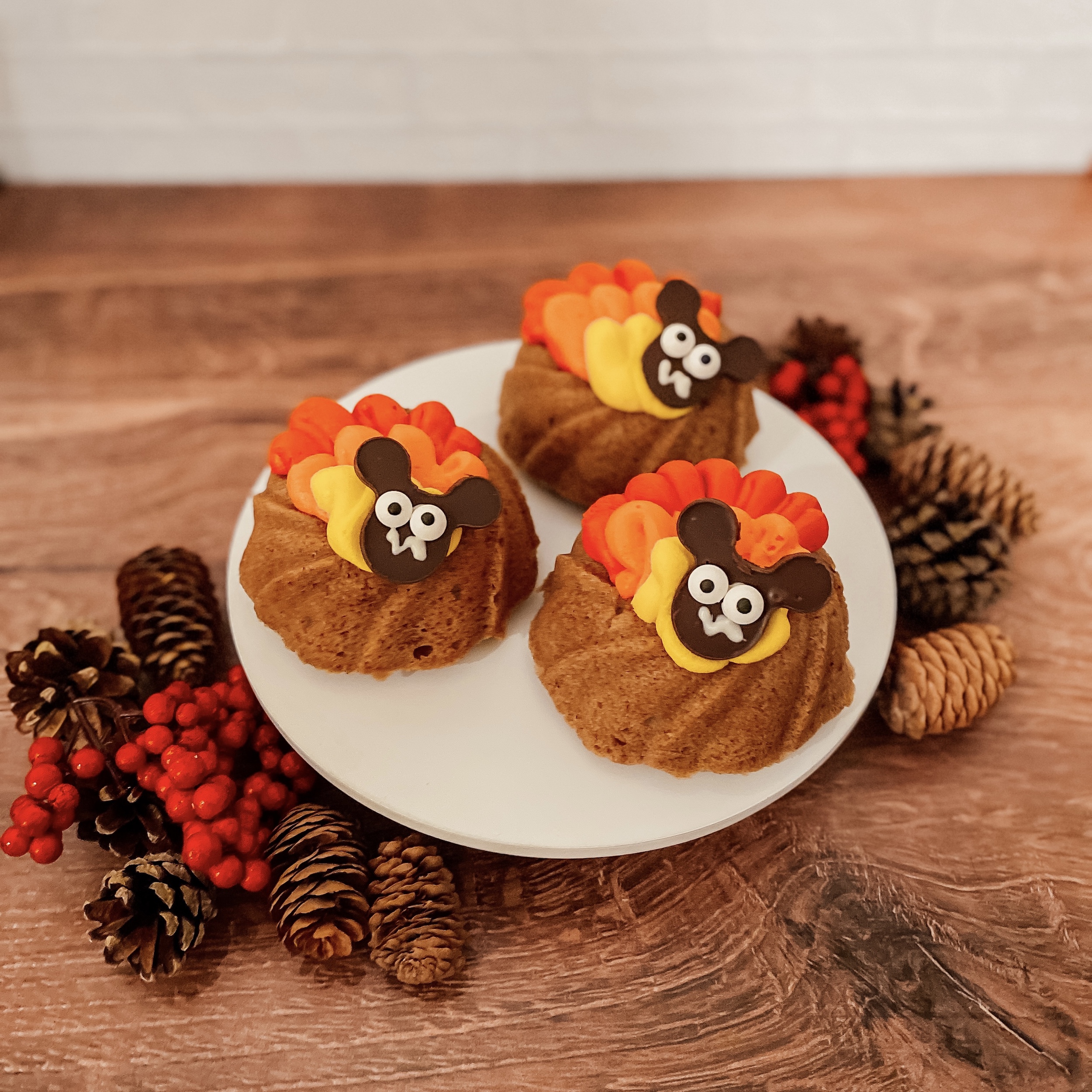 Mouseketeer Turkey Cakes (three cinnamon spice bundt cakes with red, orange, and yellow frosting, and a chocolate head with mickey ears on a plate)