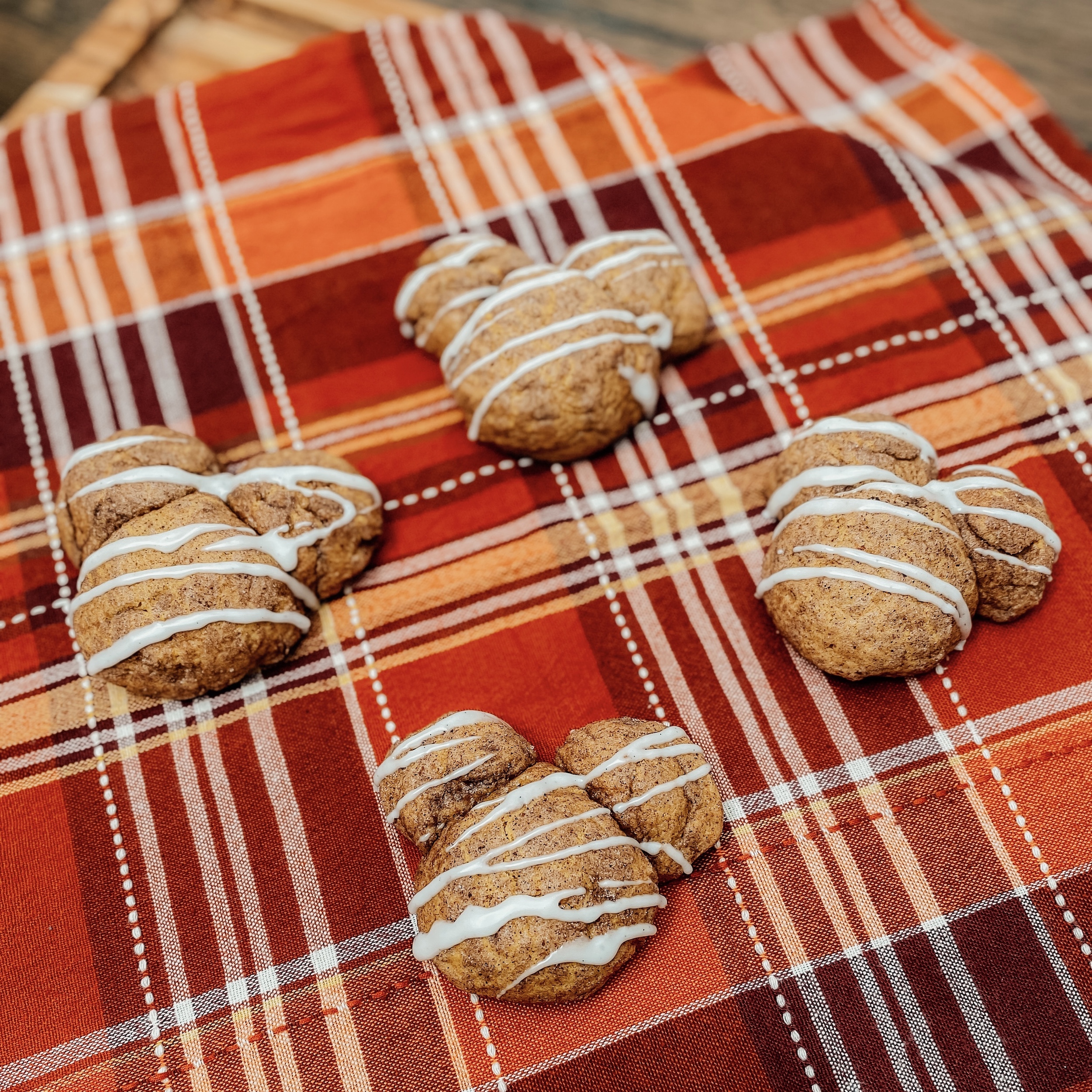 4 Pumpkin Chai Mickey Cookies (Mickey Mouse shaped pumpkin spice cookies with a vanilla glaze) on an orange and red checked tablecloth.