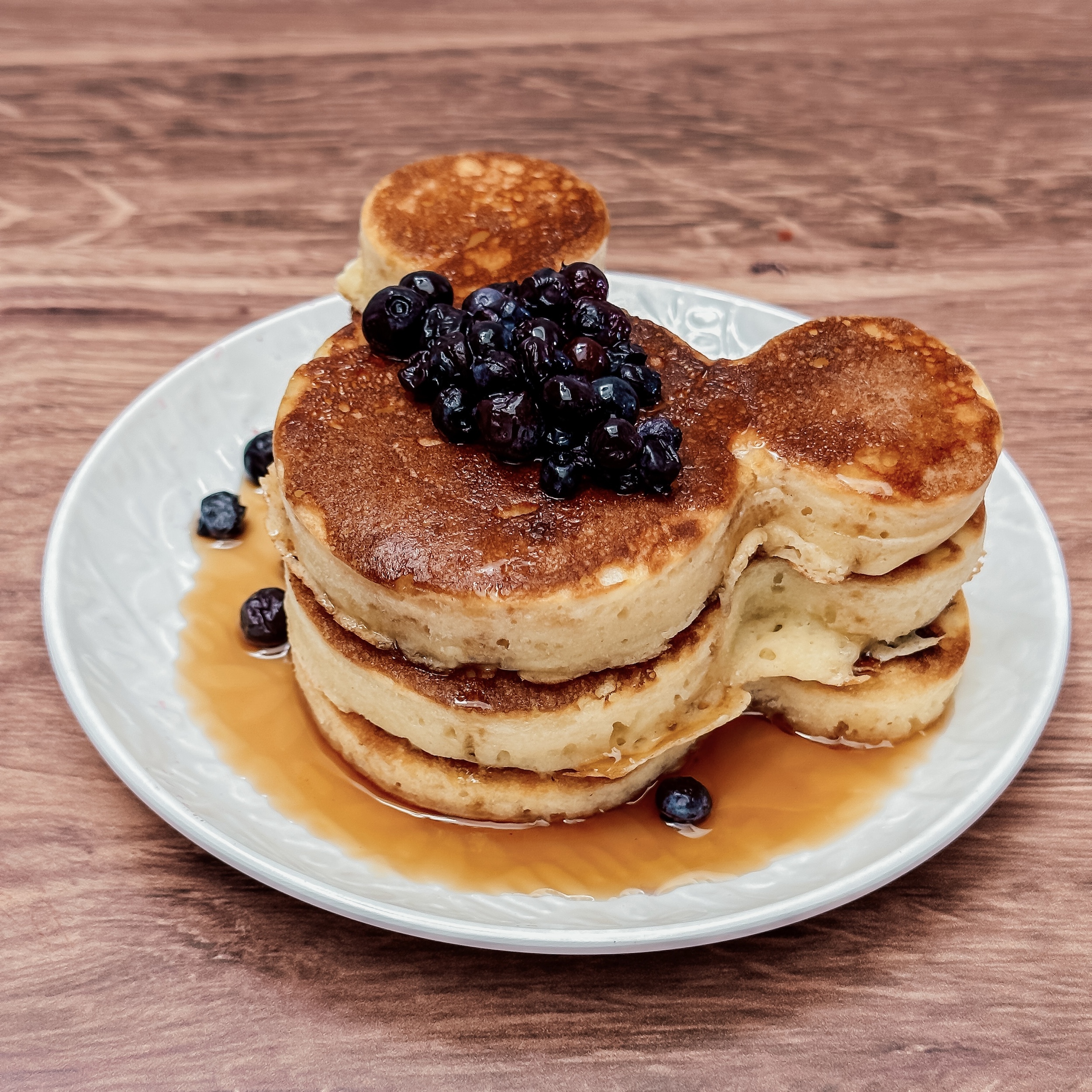 Mickey's Mardi Gras Pancakes (three mickey shaped pancakes on a plate with blueberries and syrup)