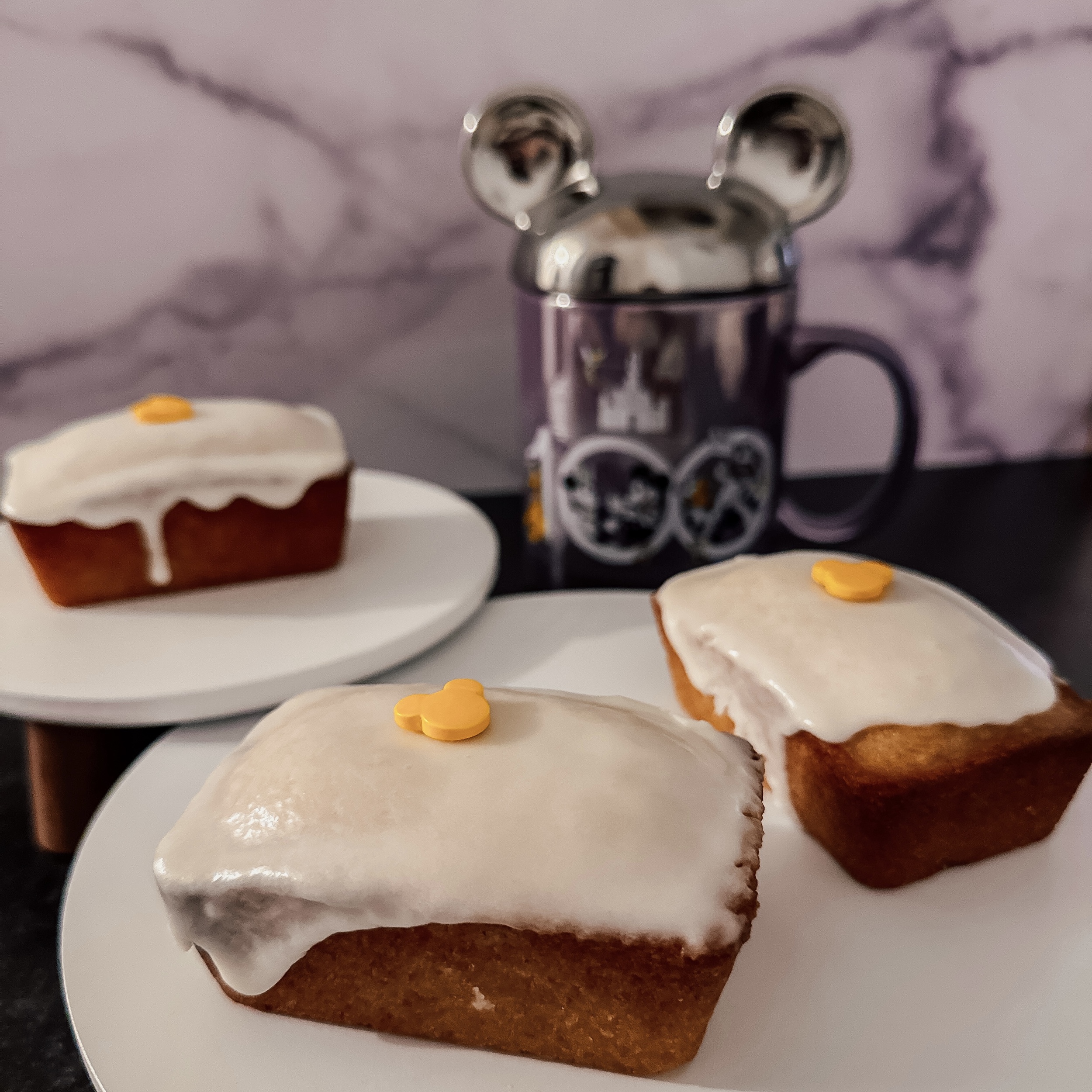 Disney100 Lemon Tea Cakes (three lemon cake loaves with white lemon icing on a tray with a Disney100 mug)